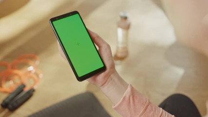 Fitness Concept: Woman Holding Chroma Key Green Screen Smartphone. In the Background Fitness Mat, Jumping Rope and Equipment. Close-up Point of View POV - Powered by Adobe