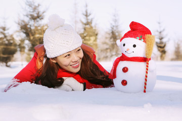 Woman in warm clothing lying on snow and looking at snowman