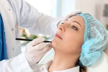 Plastic surgeon applying marks on woman's face in clinic