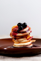 A stack of mini pancakes on a brown saucer with blackcurrant jam.