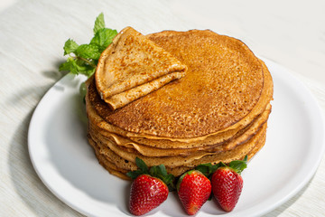 pancakes with strawberries with mint leaves and a slice of butter on a plate, morning homemade breakfast for breakfast, a white dish on a light background