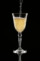 Pouring of champagne into glass on dark background