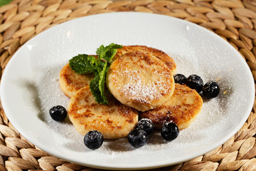 pancakes with blueberry mint leaves and powdered sugar on a plate, morning homemade breakfast for breakfast, a white dish on a straw napkin, close-up of food
