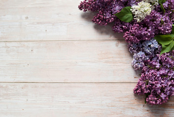 Flower composition. Border of flowers and green leaves of fragrant lilac (Syringa vulgaris) close-up on a light wooden background. Free space.