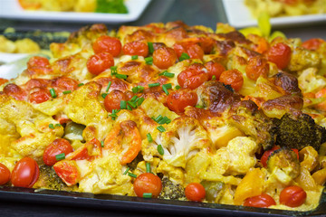 baked vegetables from the oven under cheese, a vegetarian dish of stew, on a baking sheet potatoes tomatoes cauliflower broccoli green onions zucchini