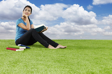 Fototapeta premium Young woman sitting on grass reading a book