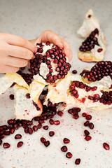 Child hands peel pomegranate on a white texture table background. Pomegranate seeds are scattered....