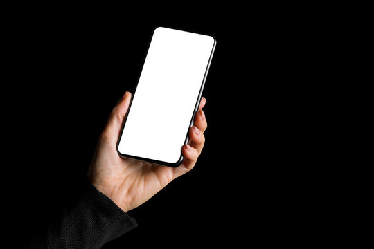 Person holding in hand mobile phone with blank white screen, isolated on black background