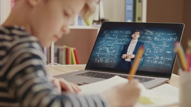 Smart Little Boy Uses Laptop for Video Call with His Teacher. Screen Shows Online Lecture with Teacher Explaining Subject from a Classroom, Boy writes Down Information. E-Education Distance Learning