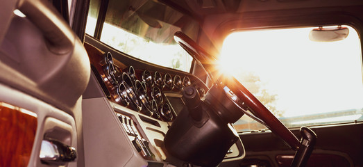 Classic american commercial semi truck with stylish chrome gauges panel and custom luxury wooden steering wheel. Luxurious and comfortable cabin of 18 wheeler truck at evening, back lit, warm filter. © Moab Republic