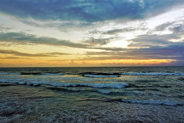 Fototapeta na wymiar Magical sunset over the Indian Ocean. The waves slowly roll towards the shore, adorned with foam. The clouds are painted with the sun, like watercolors in pink, orange, gold, blue, turquoise. Amazing 