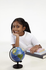 Girl smiling with hand resting on books and a globe on the table