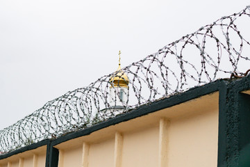 The dome with the cross of the Church on the background of barbed wire