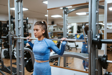 Fototapeta na wymiar A young beautiful caucasian woman in blue sports equipment lifts weights in the gym