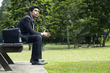 Obraz premium Young Asian businessman sitting on a park bench