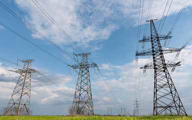 High-voltage power lines passing through a green field of wheat, on the background of a cloudy sky
