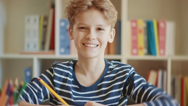 Happy Little Boy Does Homework, Writes Down Useful Information, Looks at Camera and Smiles. Distance Learning, e-Education, e-Learning, Homeschooling Concept. Portrait of a Boy Doing Homework