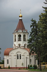 Fototapeta na wymiar A chapel with a gilded dome on the territory of an Orthodox Church against a cloudy sky next to fir trees