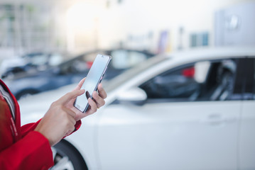A female car salesman is using a phone to contact customers to sell a new car in the car showroom. Selling cars online