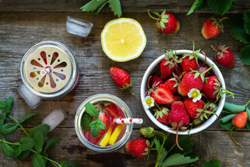 Refreshing Summer drink. Lemonade with fresh strawberries, ice and lemons on a rustic wooden table. Top view flat lay background.