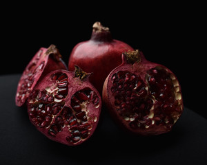 close up of a fruit still life, pomegranates cut open on a black studio background.