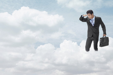 Young businessman standing on clouds, looking below