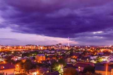 View of the illuminated night city with a TV tower in the distance with cloudy skies
