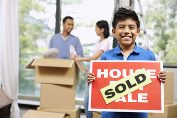 Boy holding For Sale sign with SOLD on it, man and woman packing in the background