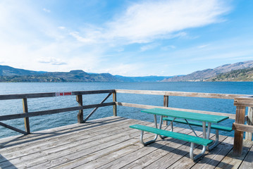 Picnic table on Naramata Wharf with scenic view of Okanagan Lake, mountains, and blue sky