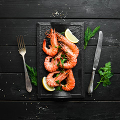 Boiled shrimp with parsley and lemon on a black stone plate. Top view. Seafood.