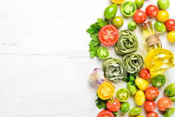 Raw green pasta with tomatoes, oil and parsley on white wooden background. Italian traditional cuisine. Fresh vegetables. Top view. Free space for your text.