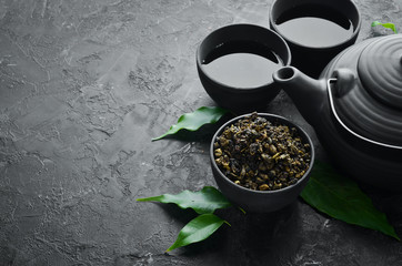 Chinese green tea in a cup with a kettle. On a black stone background. Top view. free space for your text.