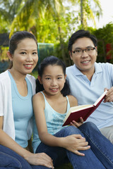 Girl reading book in the park with her parents