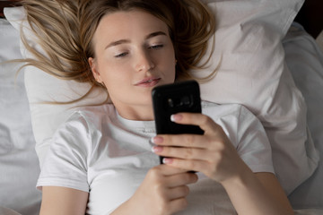 Closeup portrait of a young woman in bed. Mobile phone in the hands.