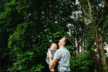 Father throws baby in nature, girl flies in the sky. Portrait dad with child together. Daddy, little daughter outdoors. Young father with baby girl walk in park. Family holiday in garden or forest.