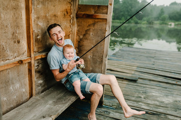 Family fishing holiday. Father with daughter sitting on wooden pier and catching fish on lake...