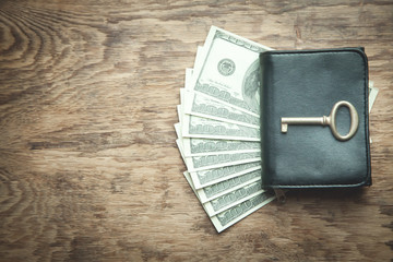 Old key, wallet and dollars on the wooden background.