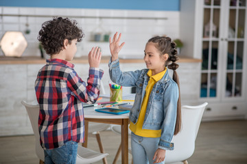 Dark-haired girl and curly boy smiling, giving high five to each other