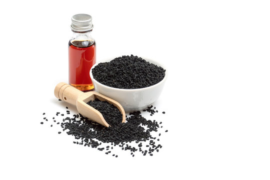 Black cumin seeds in bowl and essential oil in glass bottle. Nigella sativa isolated on white background.