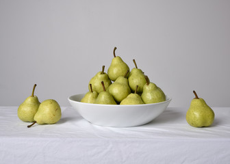 close up portrait of group of green pears on white table cloth against a studio background.