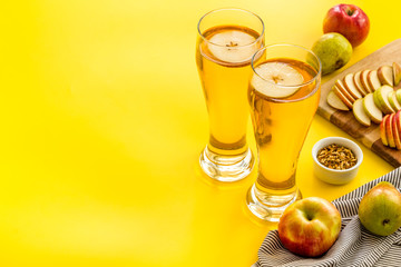 Glasses of beer with apple and peer on yellow table copy space