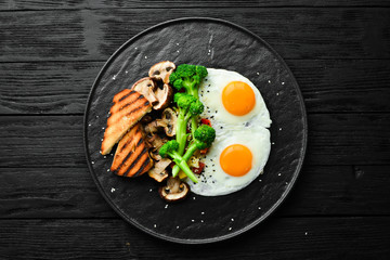 Healthy breakfast. Fried egg with broccoli, mushrooms and bread. On a black stone plate. Top view.