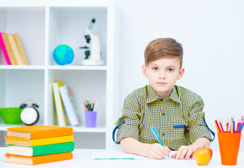 A boy sitting at a table at home in front of a notebook for lessons. Boy smiling at camera