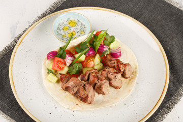 Lamb shish kebab cooked in a josper oven. Served on a plate with pita bread, vegetables and sauce.