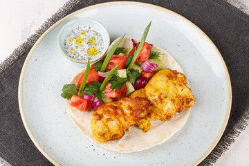 Chicken skewers cooked in a josper oven. Served on a plate with pita bread, vegetables and sauce.