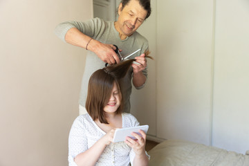 Caucasian dad learns to comb and trim daughter’s hair online. Father cuts the hair of a child to...