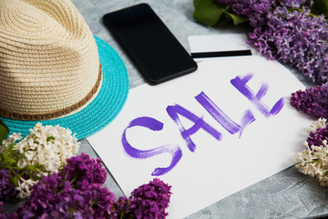 Handwritten word sale in white frame, smartphone, credit card lay in lilac blossom. Shopping concept.