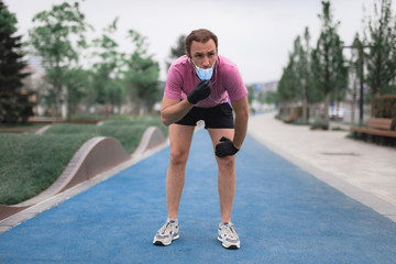 Sportsman with medical mask and gloves, smartphone and earbuds working out, jogging in urban surroundings.