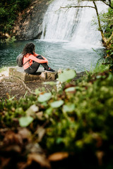 Woman sitting by the river watching a waterfall
