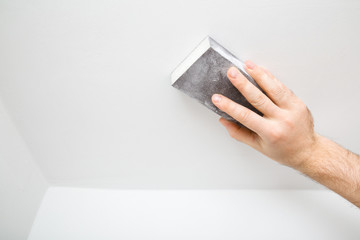Worker hand polishing white ceiling with sanding sponge. Closeup.